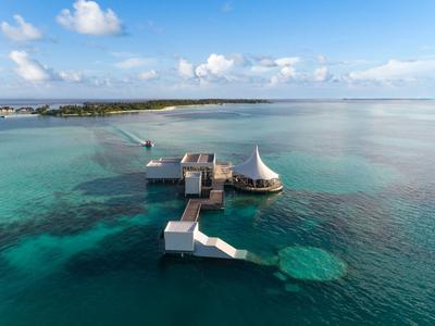 Pohled na resort na kůlech nad tyrkysovou vodou s molem a jasnou oblohou.