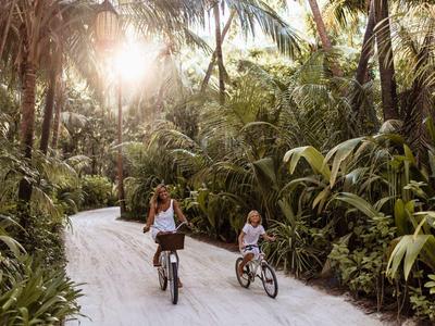 Kobieta i dziecko jadą rowerami po ścieżce otoczonej tropikalną roślinnością.