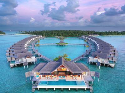 Luftaufnahme von tropischen Wasserbungalows in Herzform umgeben von türkisblauem Meer.