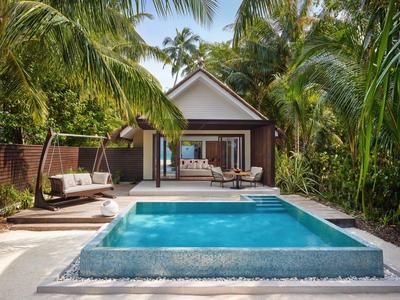Nowoczesny domek przy basenie otoczony palmami i tropikalną roślinnością z miejscami do siedzenia przy basenie.