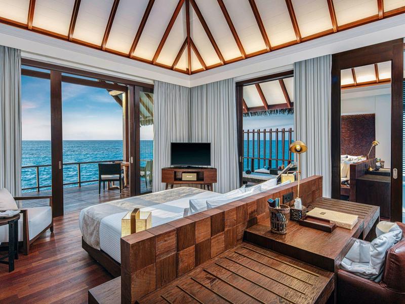 Luksusowy pokój hotelowy z widokiem na morze, dużym łóżkiem, drewnianymi meblami i otwartym balkonem z balustradą.