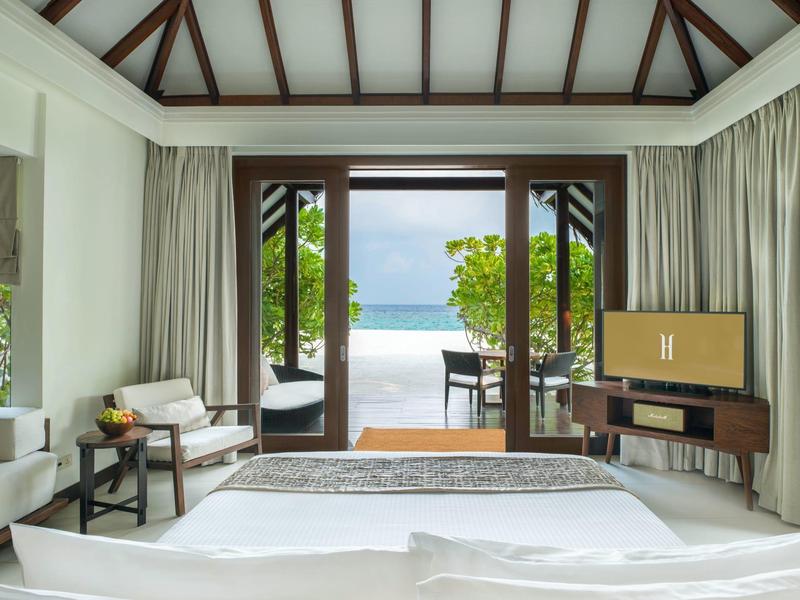 Jasna sypialnia z widokiem na taras, ogród i morze przez duże drzwi.