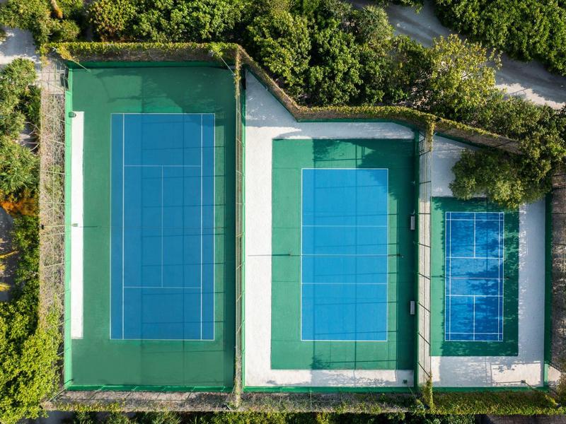 Trzy korty tenisowe o różnych rozmiarach otoczone drzewami i ścieżkami.