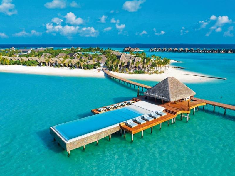 Bungalow na wodzie z basenem typu infinity w turkusowej wodzie przy tropikalnej wyspie z palmami.