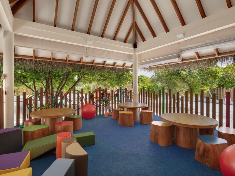 Zadaszony teren na zewnątrz z siedziskami z pni drzew i kolorowymi poduszkami pod drewnianą konstrukcją dachu.