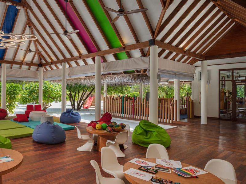 Nowoczesny, kolorowy salon hotelowy z różnorodnymi miejscami do siedzenia i wysokimi drewnianymi sufitami.