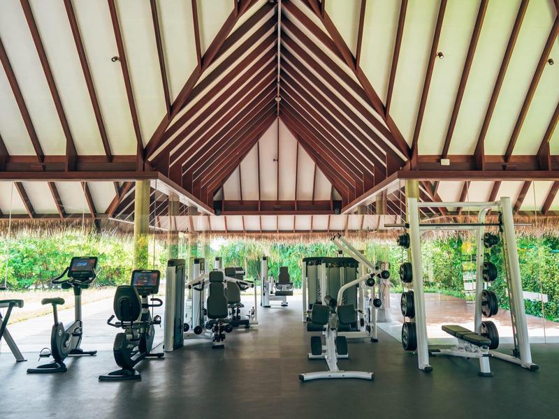 Jasna siłownia z nowoczesnym sprzętem i widokiem na zielone tereny na zewnątrz.