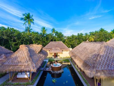 Tropisches Resort mit Strohdach-Bungalows, zentralem Pool und Palmen vor blauem Himmel.