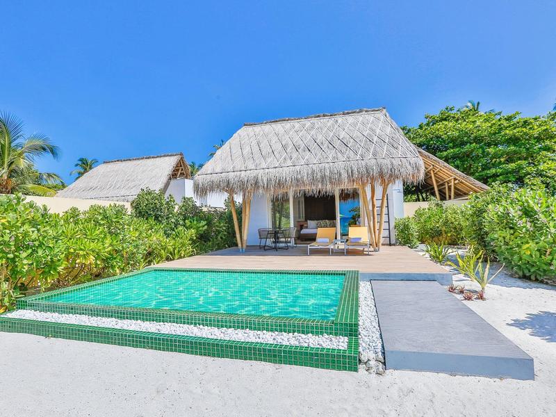 Modernes Strandbungalow mit privatem Pool und tropischer Vegetation unter klarem Himmel.