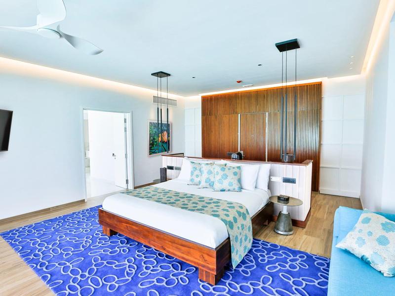 Modernes Schlafzimmer mit großem Bett, blauem Teppich und hellen Wänden.