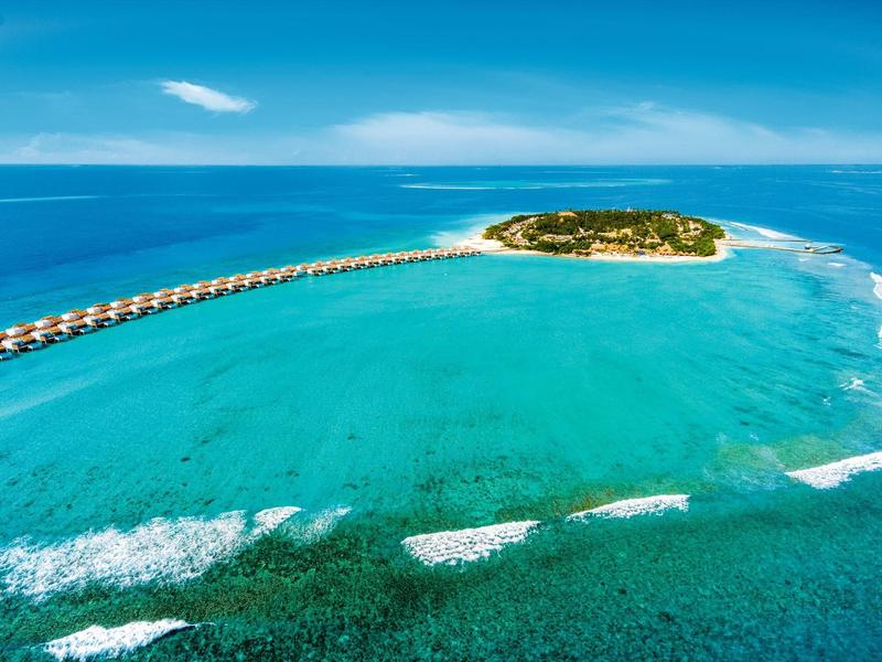 Luxuriöse Wasservillen auf Stelzen führen zu einer kleinen tropischen Insel im türkisblauen Ozean.