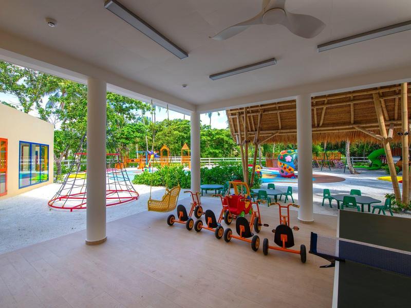 Kinderspielbereich mit Kleinkindern, Rutschen und freiem Platz unter einem überdachten Bereich.