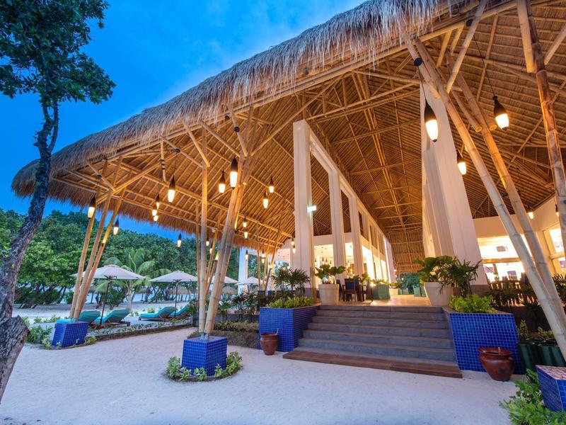 Strandresort mit Strohdach, Hängebeleuchtung und Treppe zum Eingang bei Abenddämmerung.