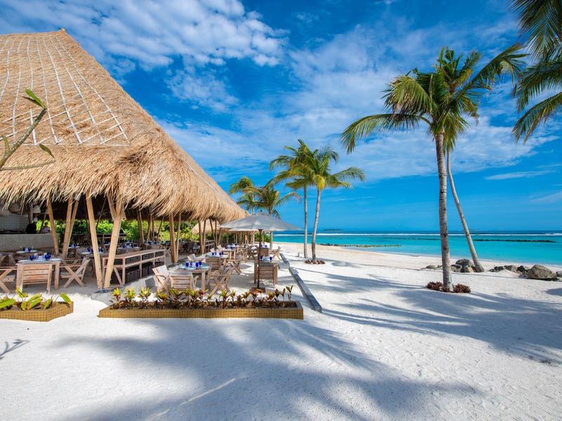 Strandrestaurant mit Strohdach, weißen Sandstränden und Palmen bei blauem Himmel.