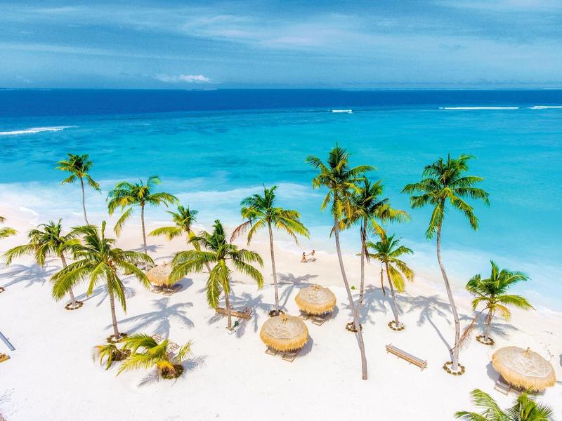 Weißer Sandstrand mit Palmen und Sonnenschirmen am klaren blauen Meer.