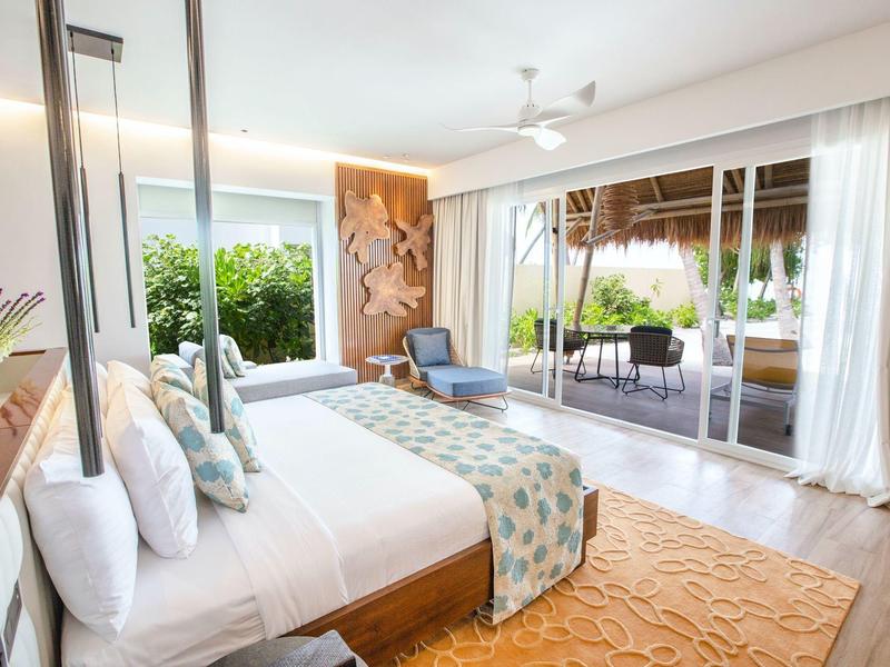 Helles Hotelzimmer mit Doppelbett, Terrasse und Blick auf einen Garten.