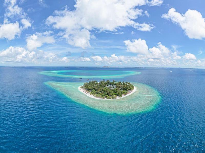 Klein tropisch eiland omgeven door kristalhelder blauw water onder een blauwe lucht.