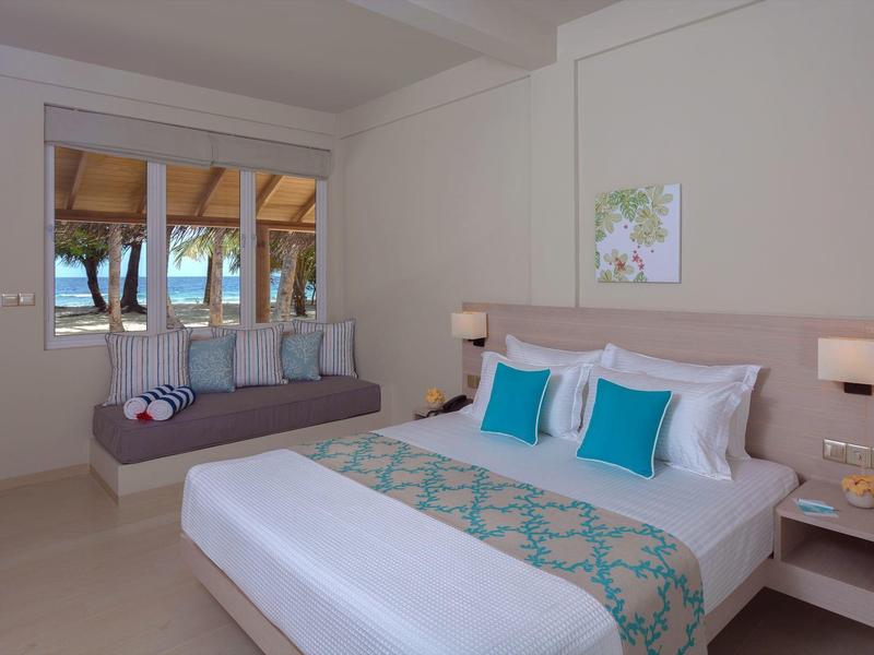 Modern hotelkamer met groot bed, bank en raam met uitzicht op zee.