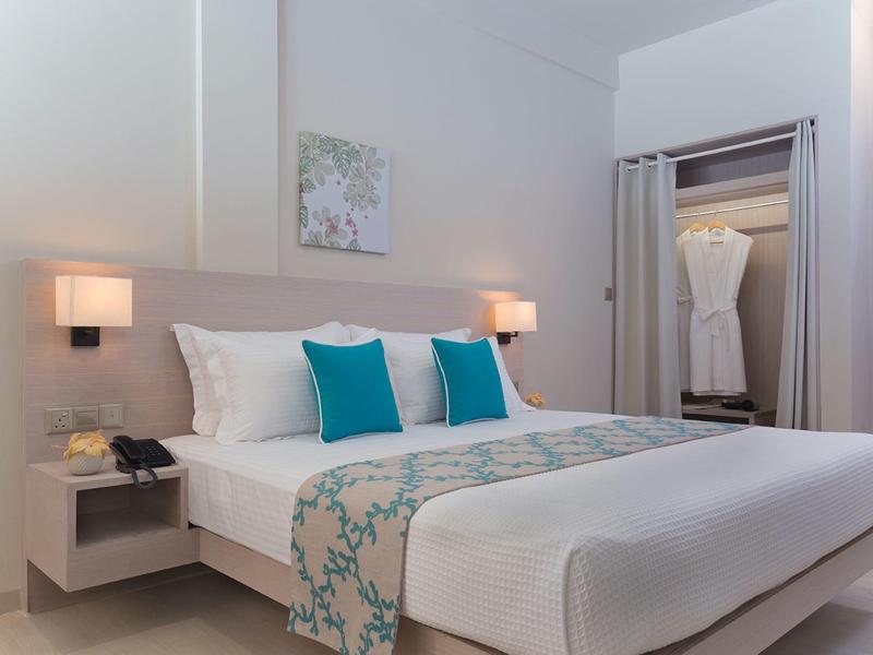 Modern hotelkamer met tweepersoonsbed, wit beddengoed en blauwe accentkussens.