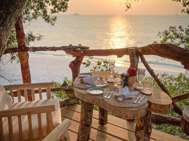 Gezellig buiten eetgedeelte met uitzicht op zee bij zonsondergang.