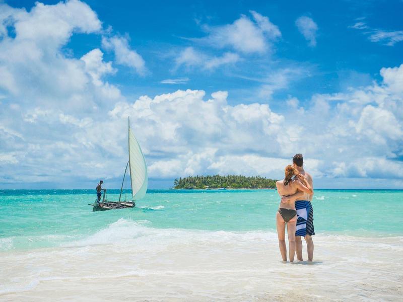 Familie op wit zandstrand met helderblauw water en zeilboot in de verte