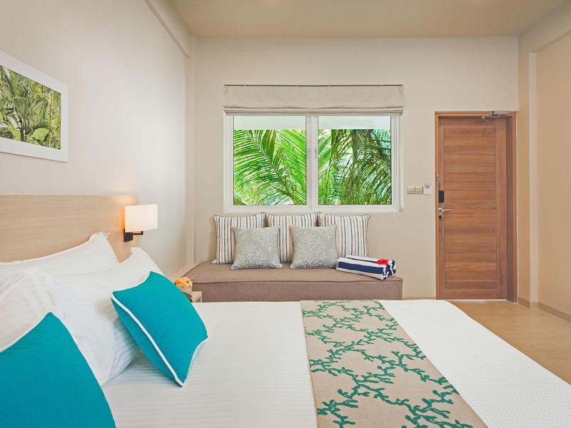 Lichte slaapkamer met groot bed, vensterzitje en uitzicht op groene bladeren.