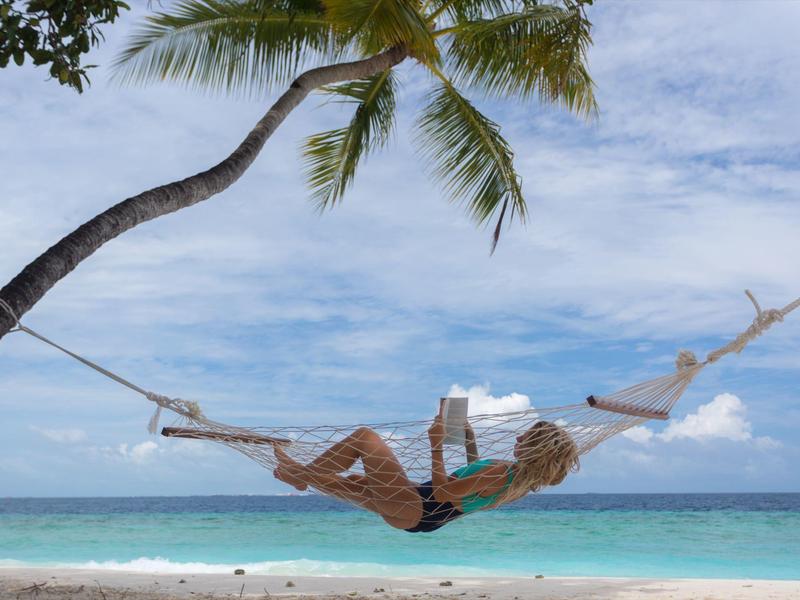 Persoon ontspant in een hangmat onder palmbomen op een tropisch strand met turquoise zee.