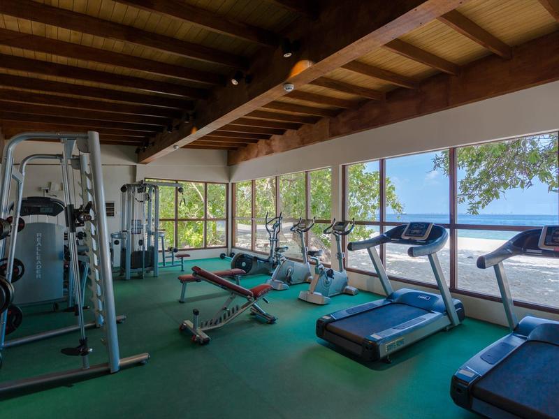 Fitnessruimte met apparatuur en grote ramen met uitzicht op zee.