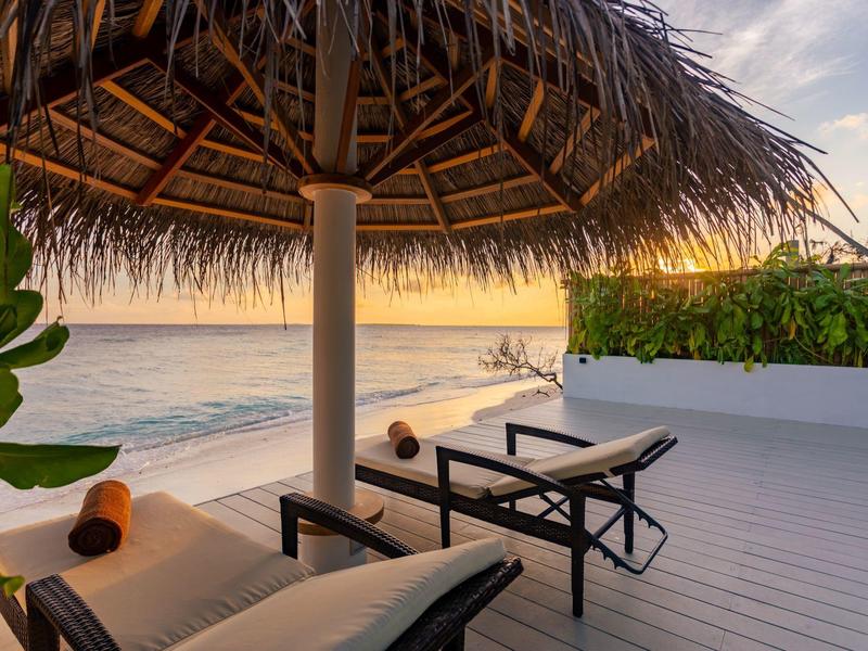 Twee ligstoelen onder een rieten dak met uitzicht op zee bij zonsondergang.