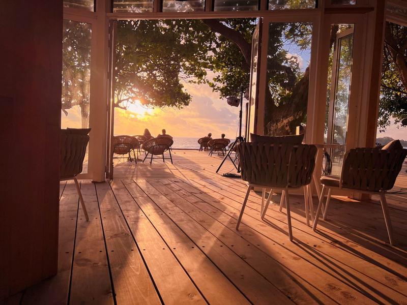 Zitgedeelte met stoelen en tafels op een terras met uitzicht op de zonsondergang bij de zee.