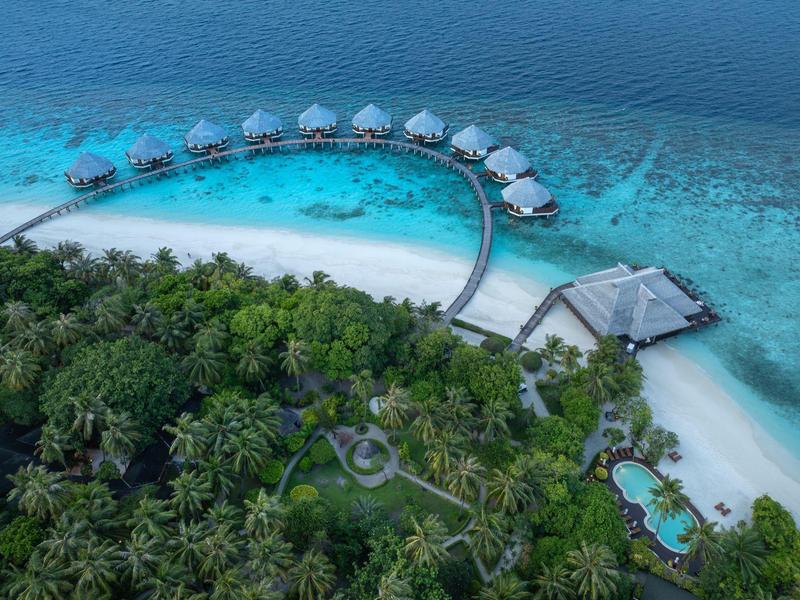 Overzicht van een luxe resort aan zee met waterbungalows en tropisch bos.