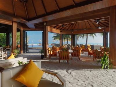 Lounge all'aperto con pavimento sabbioso, mobili in legno e vista sul mare e le palme.