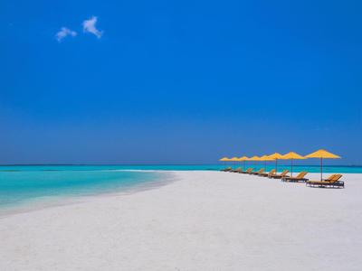 Weißer Sandstrand mit klarem türkisfarbenem Wasser und gelben Sonnenschirmen unter blauem Himmel