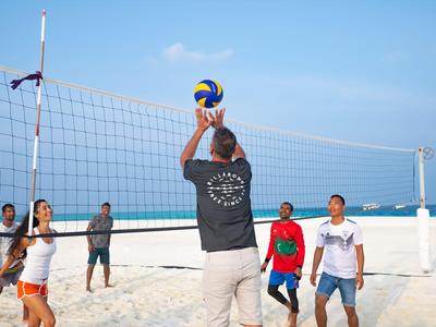 Gruppe spielt Beachvolleyball bei Tageslicht am Strand vor Meereshorizont.
