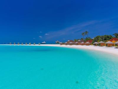 Türkisfarbenes Meer und weißer Sandstrand mit Sonnenschirmen und Palmen unter blauem Himmel.