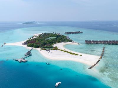 Isola tropicale con spiaggia di sabbia bianca, vegetazione rigogliosa e bungalow sull'acqua nel mare azzurro.