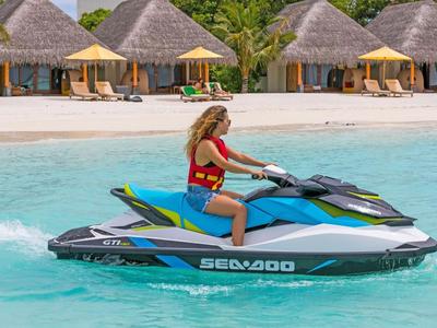 Frau auf einem Sea-Doo Wassermotorrad im klaren blauen Wasser vor Bungalows mit Strohdächern