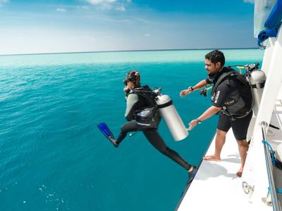 Ein Taucher springt vom Boot ins klare blaue Wasser, begleitet von einem weiteren Taucher an Bord.