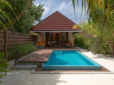 Piccola casa tradizionale con tetto rosso e piscina circondata da piante tropicali.