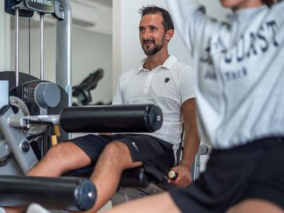 Zwei Personen trainieren in einem hellen Fitnessraum mit modernen Geräten.