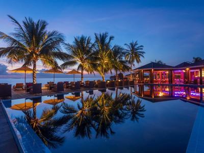 Luxuriöser Poolbereich mit Palmen und stimmungsvoller Beleuchtung bei Sonnenuntergang.