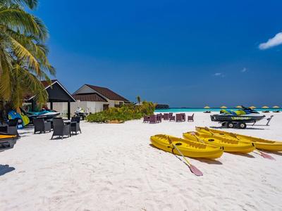 Strand mit Kajaks, Liegestühlen und Strandhütten bei klarem Himmel.
