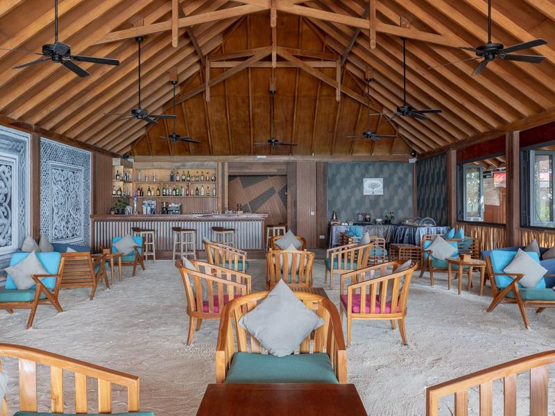 Accogliente sala lounge dell'hotel con mobili in legno, cuscini e soffitto aperto con ventilatori.