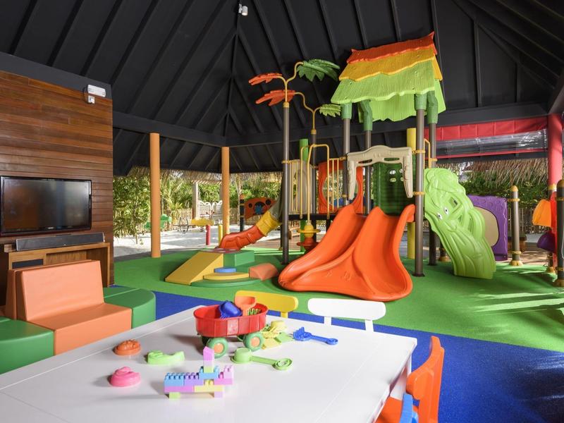 Area bambini con parco giochi colorato, scivoli e tavolo per attività manuali in una sala giochi dell'hotel.