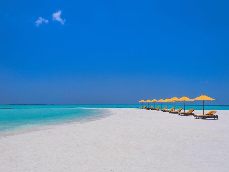 Spiaggia di sabbia bianca con acqua turchese e ombrelloni gialli sotto un cielo azzurro limpido.