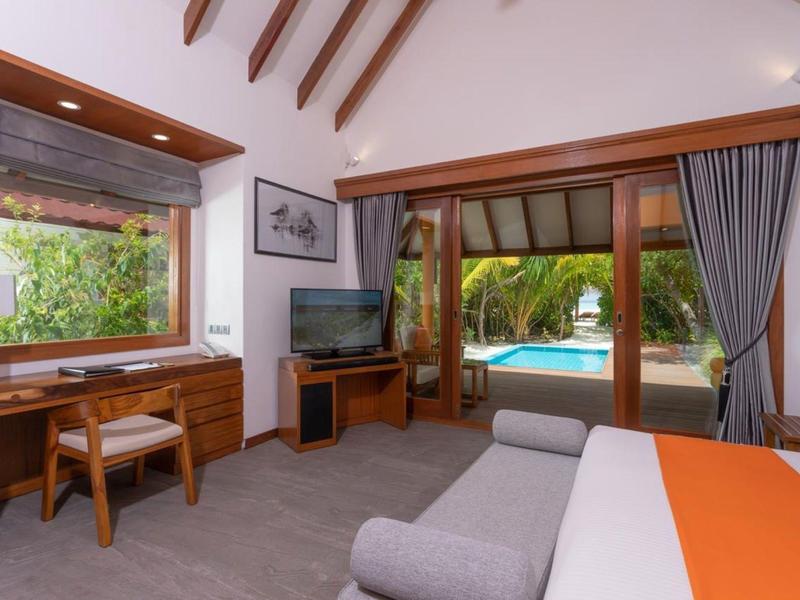 Camera d'hotel elegante con mobili in legno, TV e vista sulla piscina attraverso grandi finestre.