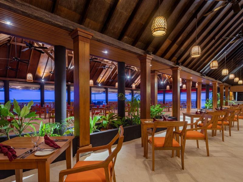 Ristorante aperto con mobili in legno e piante che creano un'atmosfera rilassata al crepuscolo.