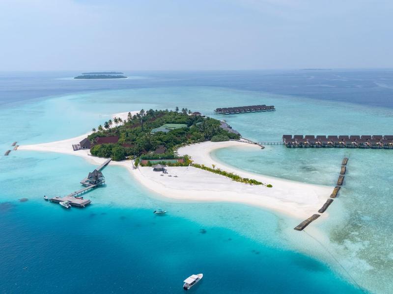 Isola tropicale con spiaggia di sabbia bianca, vegetazione rigogliosa e bungalow sull'acqua nel mare azzurro.