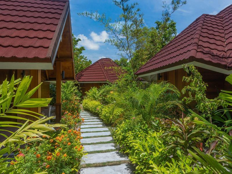 Sentiero in piastrelle di pietra attraversa un giardino rigoglioso verso case dai tetti rossi.