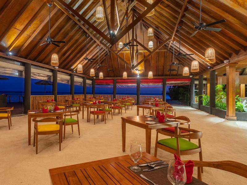 Area ristorante aperta con tetto in legno e lampadari moderni in hotel di notte.